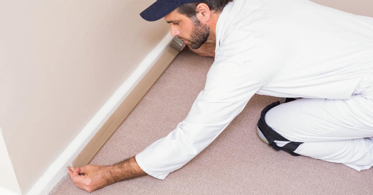 Homme agenouillé protégeant une plinthe avec du scotch avant de peindre.
