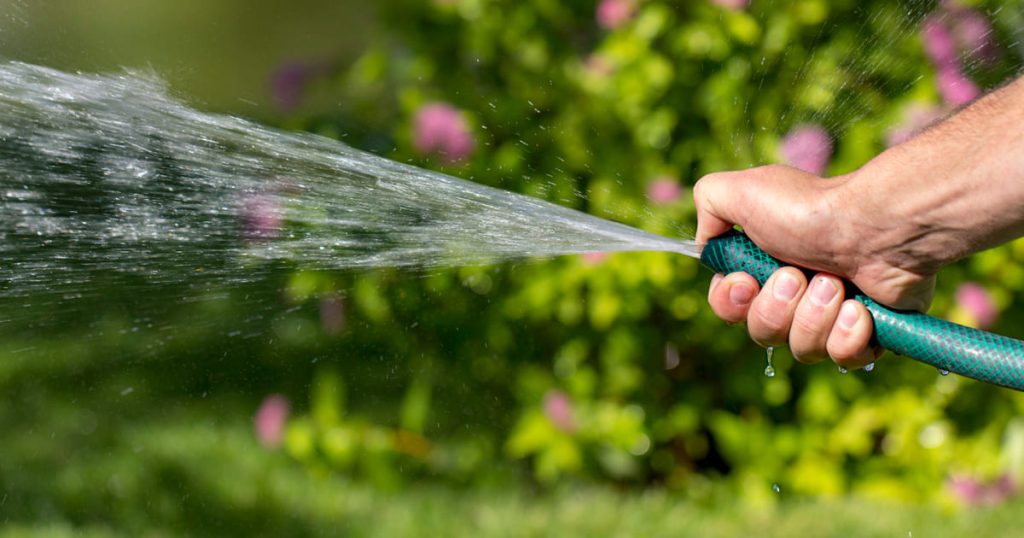 Une main tient un tuyau d'arrosage avec de l'eau qui coule.